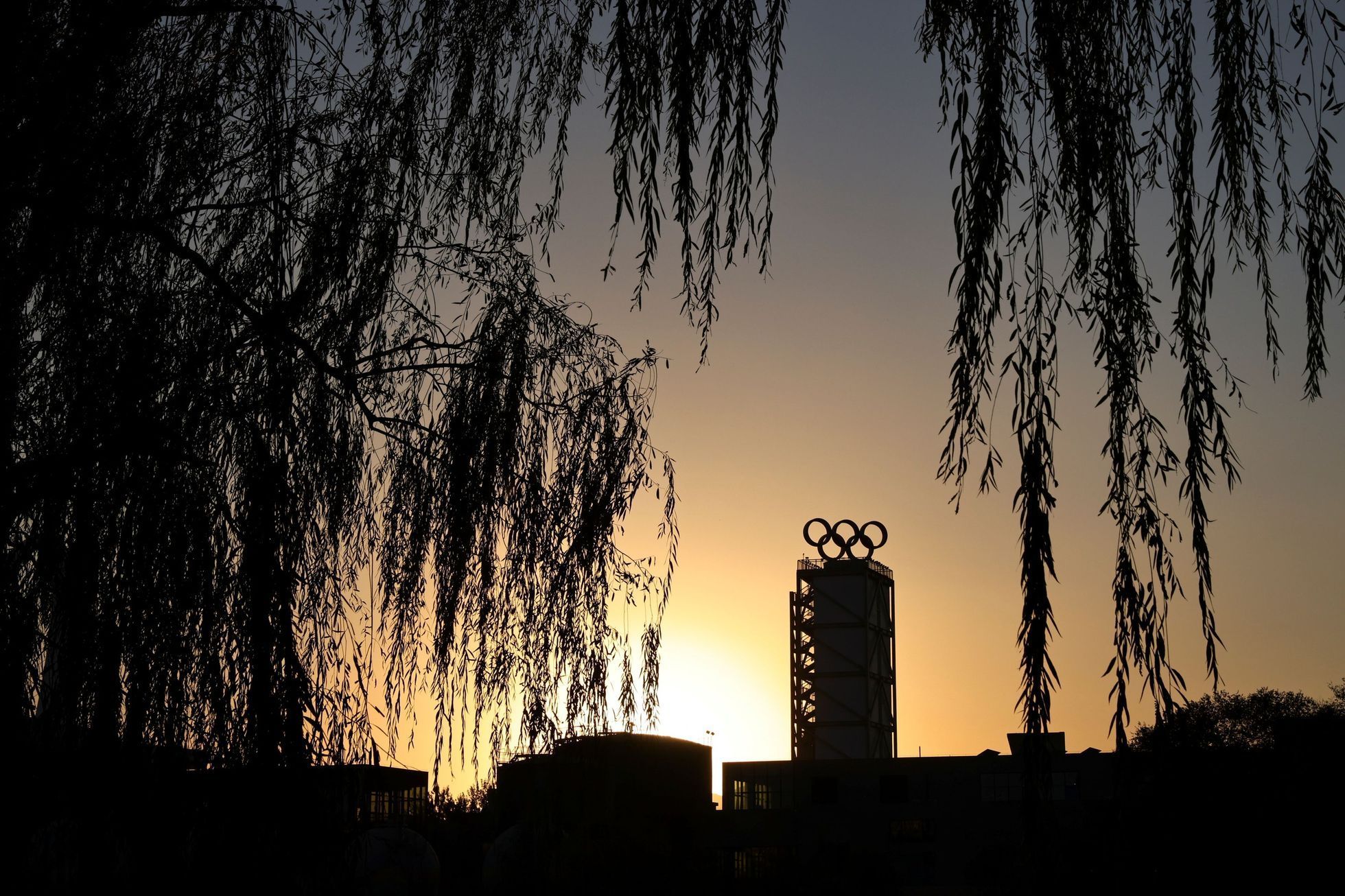 The sun sets behind a building topped with the Olympic rings, in Beijing
