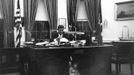 Former United States President John F. Kennedy sits as his desk in the Oval Office while his son, John F. Kennedy Jr., looks out from underneath, at the White House in Washington in this handout image taken on October 17, 1963.