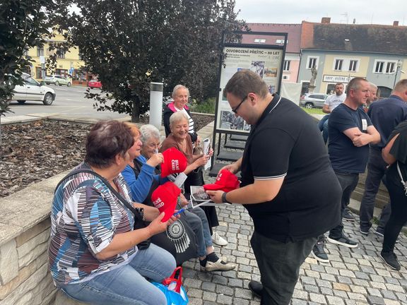 Seniorky v Přešticích si berou kšiltovky hnutí ANO, které jim rozdává jeden ze spoluorganizátorů mítinku.