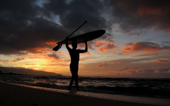 Surfař se svým prknem na pláži Waialua na pobřeží Havajského Oahu.