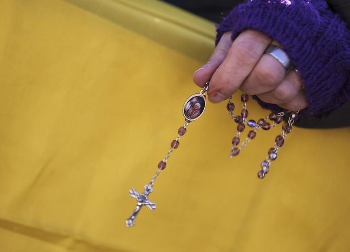 A woman in the crowd holds a small cross before the arrival of Pope Benedict XVI at his last general audience at St Peter's Square at the Vatican February 27, 2013. The weekly event which would normally be held in a vast auditorium in winter, but has been moved outdoors to St. Peter's Square so more people can attend. The pope has two days left before he takes the historic step of becoming the first pontiff in some six centuries to step down instead of ruling for life. REUTERS/Alessandro Bianchi (VATICAN - Tags: RELIGION) Published: Úno. 27, 2013, 10:19 dop.