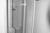 Koupelna působila stísněně, měla malý sprchový kout, umyvadlo a věšáky na dveřích.