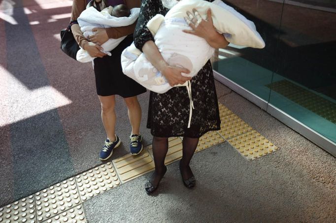 Ward officials, who did not want to be identified, hold abandoned babies as they head to a child advocacy centre after the babies had undergone checkups at a children's hospital in Seoul September 19, 2012. The babies were left in a "baby box" at Joosarang church. Pastor Lee Jong-rak of the church, who runs the "baby box" where mothers can leave unwanted infants, has seen a sharp increase in the number of newborns being left there because, the pastor says, of a new law aimed protecting the rights of children. South Korea is trying to shed a reputation of being a source of babies for adoption by people abroad. It is encouraging domestic adoption and tightening up the process of a child's transfer from birth mother to adoptive parents. Picture taken September 19, 2012. REUTERS/Kim Hong-Ji (SOUTH KOREA - Tags: SOCIETY) Published: Říj. 7, 2012, 6:50 dop.