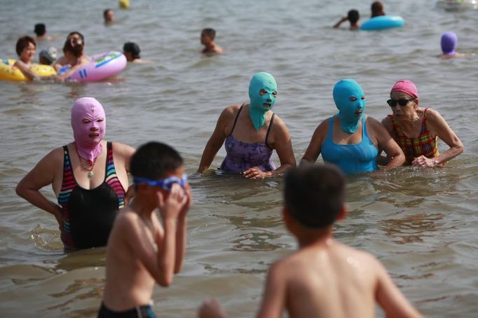 Women, wearing nylon masks, stand in the water during their visit to a beach in Qingdao, Shandong province July 6, 2012. The mask, which was invented by a woman about seven years ago, is used to block the sun's rays. The mask is under mass production and is on sale at local swimwear stores. REUTERS/Aly Song (CHINA - Tags: SOCIETY ENVIRONMENT TRAVEL) Published: Čec. 6, 2012, 4:17 odp.