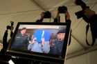 Fotografové loví snímky z televize, přenášející obraz ze soudní síně do mediálního stanu.