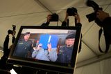 Fotografové loví snímky z televize, přenášející obraz ze soudní síně do mediálního stanu.