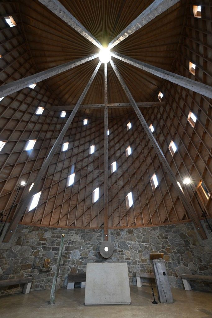 Ručně tesané trámy, dlouhé patnáct metrů, volně protínají prostor a podpírají střechu, kde vše korunuje ocelová věžička.