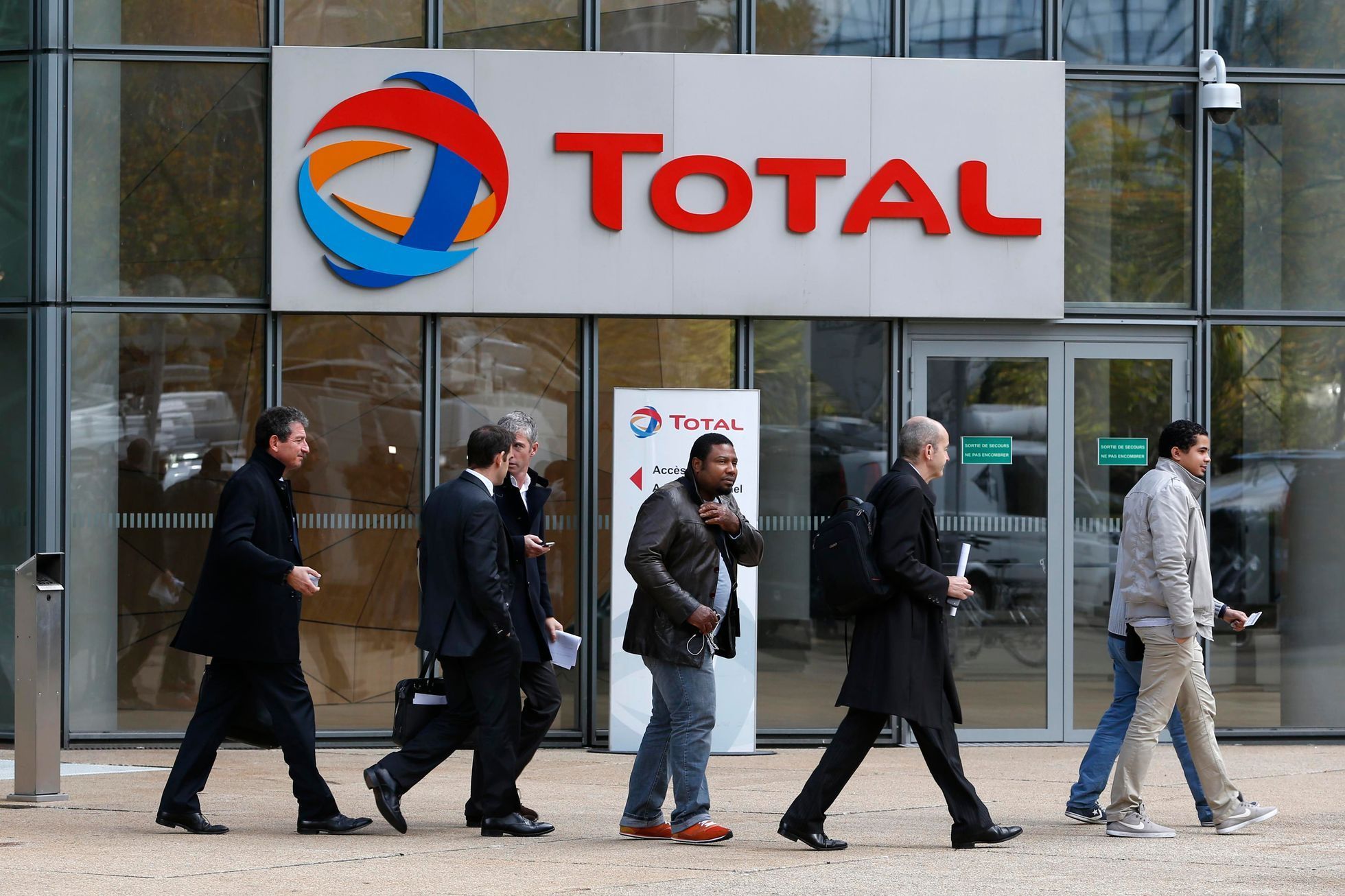 People walk past the entrance of French oil giant Total headquarters in the financial and business district of la Defense near Paris
