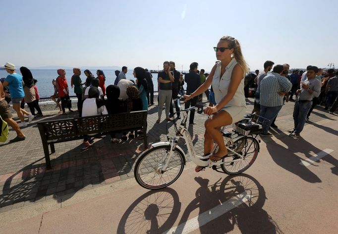 A tourist cycles past hundreds of Afghan immigrants waiting for temporary documents, which allows them to buy tickets for a ferry to Athens