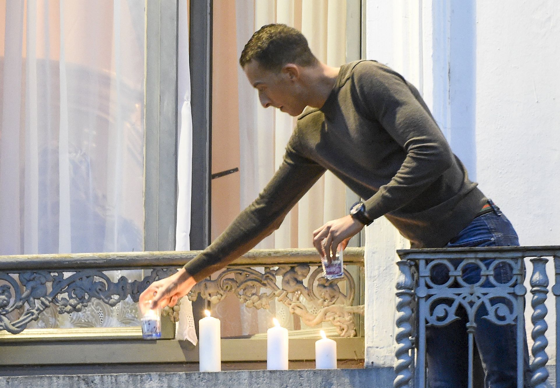 Salahův bratr Mohamed Abdeslam zapaluje na balkonu svého bytu v bruselské čtvrti Molenbeek svíčky za oběti pařížských útoků.