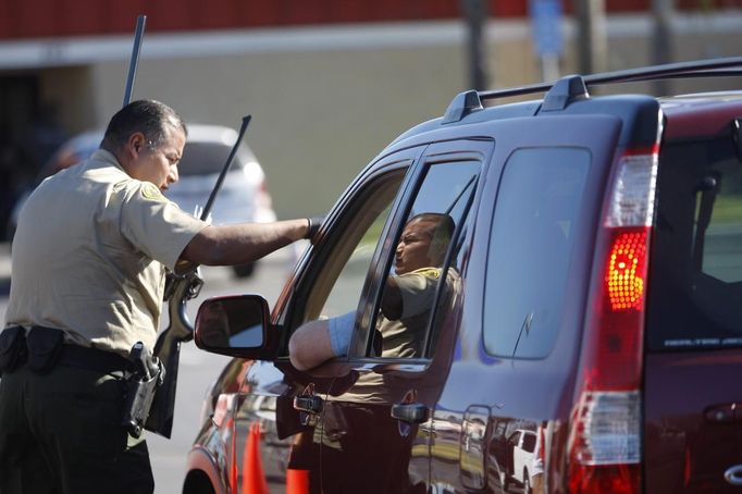 A Los Angeles County Sheriff's deputy takes in guns from motorists trading them in at the 'Gifts for Guns' gun buyback in Compton, California, January 21, 2013. People can trade in their guns anonymously and with no questions asked in exchange for $200 gift cards for assault weapons, $100 gift cards for shotguns, handguns and rifles, and $50 for non-operational firearms. U.S. President Barack Obama is pushing to address controversial issues surrounding gun violence and regulation as he begins his second term in office. REUTERS/David McNew (UNITED STATES - Tags: POLITICS SOCIETY) Published: Led. 21, 2013, 10:44 odp.