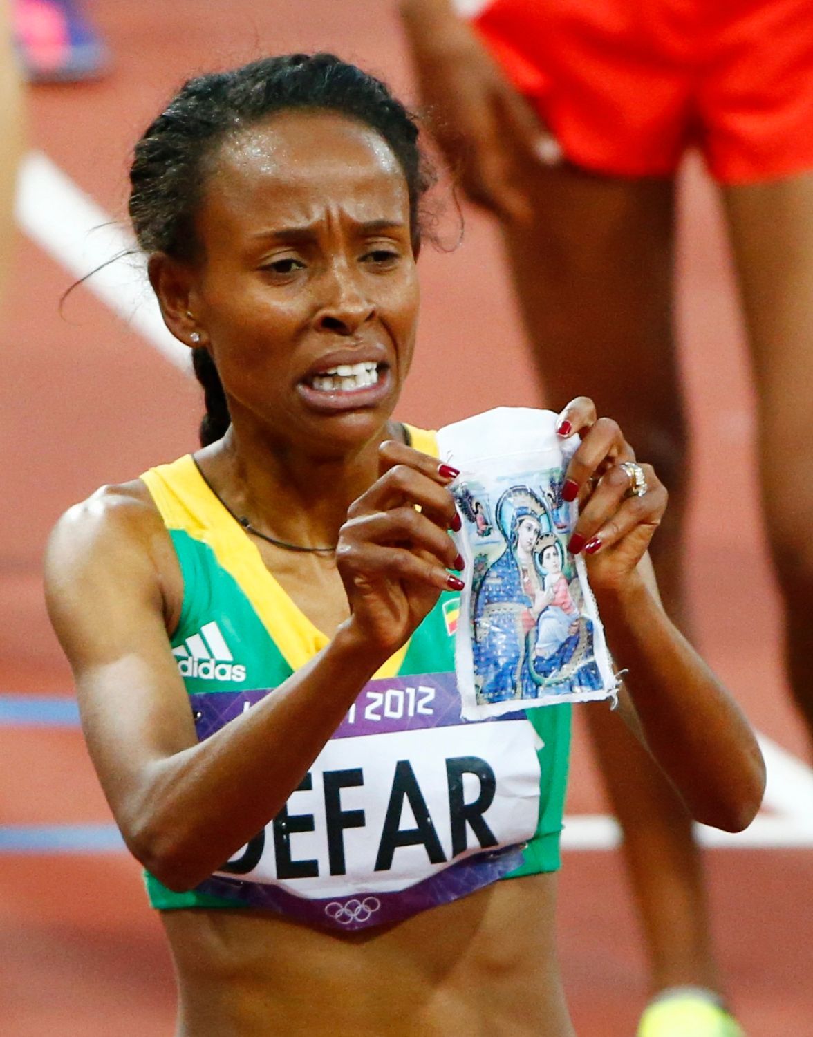 Etiopská dálková běžkyně Meseret Defarová ukazuje kousek látky s náboženskou ikonou po vítězství v běhu na 5000 metrů na OH 2012 v Londýně.