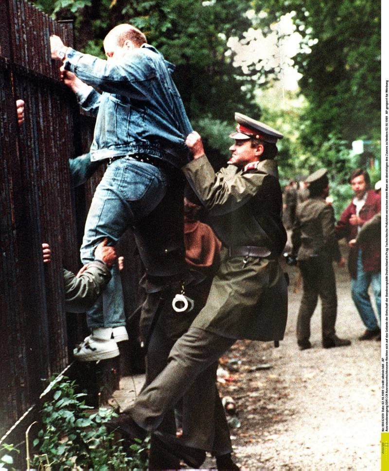 Občan NDR přelézá plot německé ambasády v Praze na podzim 1989