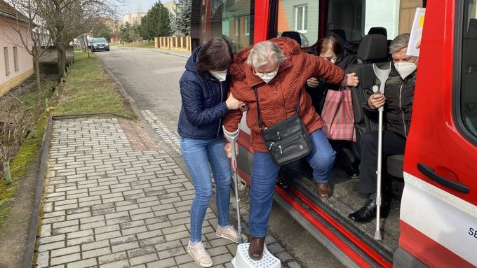 Jitka Štěpánová pomáhá vystoupit z hasičského auta jedné ze seniorek v Ostrožské Lhotě, kterou hasiči vezli na očkování proti covidu. V autě jsou i další naočkovaní senioři.