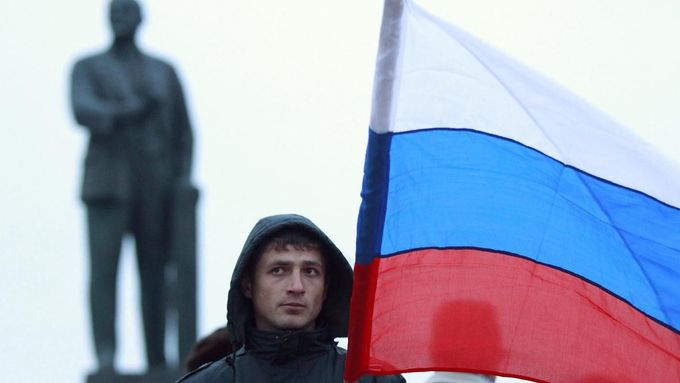 Muž drží ruskou vlajku před Leninovou sochou v Simferopolu na Krymu, 1. března 2014