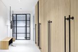 Dřevěná stěna s kovovými úchytkami, které jsou pro studio OOOOX typické, skrývají velký úložný prostor na kabáty, oblečení a potřeby do domácnosti.