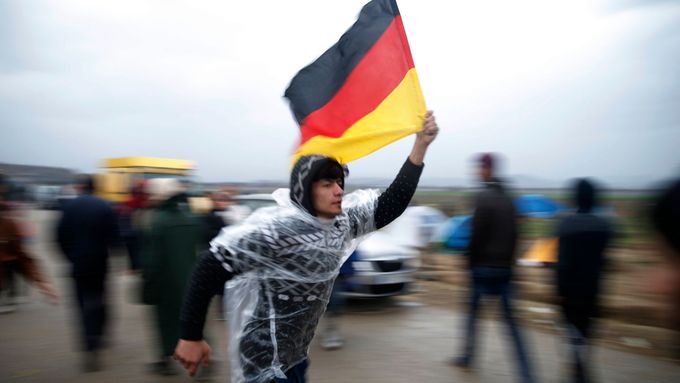 Uprchlík mává německou vlajkou na řecko-makedonském hraničním přechodu Idomeni.