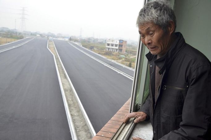 An old man looks down from his house which stands alone in the middle of a newly built road in Wenling, Zhejiang province, November 22, 2012. An elderly couple refused to sign an agreement to allow their house to be demolished. They say that compensation offered is not enough to cover rebuilding costs, according to local media. Their house is the only building left standing on a road which is paved through their village. REUTERS/China Daily (CHINA - Tags: SOCIETY POLITICS) CHINA OUT. NO COMMERCIAL OR EDITORIAL SALES IN CHINA Published: Lis. 22, 2012, 8:36 dop.