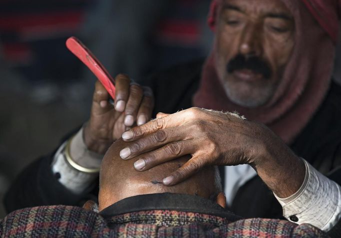 A barber shaves the head of a Hindu devotee on the banks of the river Ganges ahead of the "Kumbh Mela", or Pitcher Festival, in the northern Indian city of Allahabad January 10, 2013. During the festival, hundreds of thousands of Hindus take part in a religious gathering at the banks of the river Ganges. The festival is held every 12 years in different Indian cities. REUTERS/Ahmad Masood (INDIA - Tags: SOCIETY RELIGION) Published: Led. 10, 2013, 8:29 dop.