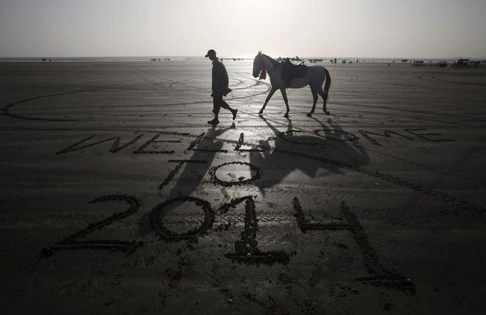 Muž jde po pláži poblíž pákistánského Karáči kolem nápisu Vítejte v roce 2014.