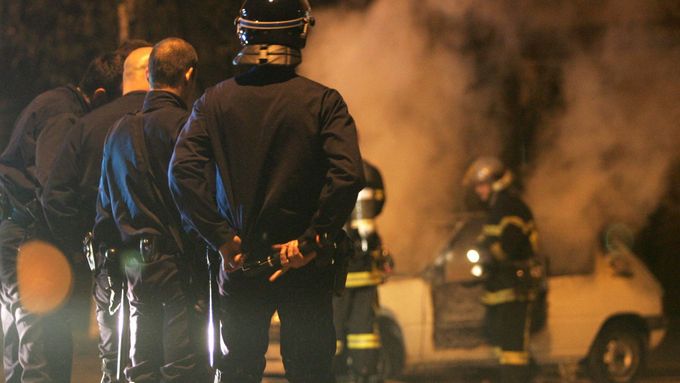 Francouzští policisté sledují práci hasičů, kteří se snaží uhasit hořící auto během čtvrteční noci ve Štrasburku.