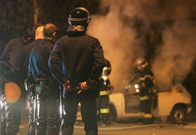 Francouzští policisté sledují práci hasičů, kteří se snaží uhasit hořící auto během čtvrteční noci ve Štrasburku.