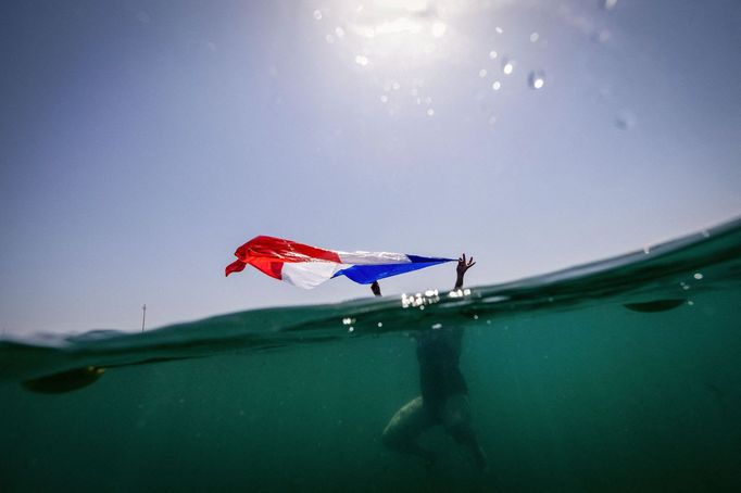 Paris 2024 Olympics - Sailing - Women's Windsurfing - Marseille Marina, Marseille, France - July 31, 2024. A supporter of France waves the national flag as she swims befo