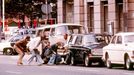 Policisté v civilu se kryjí za auty na náměstí Norrmalmstorg ve Stockholmu 23. srpna 1973, kde lupiči drželi rukojmí při neúspěšném pokusu o vyloupení banky.