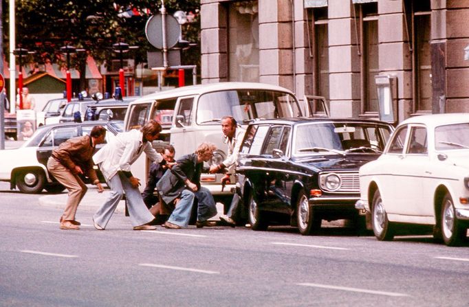 Policisté v civilu se kryjí za auty na náměstí Norrmalmstorg ve Stockholmu 23. srpna 1973, kde lupiči drželi rukojmí při neúspěšném pokusu o vyloupení banky.