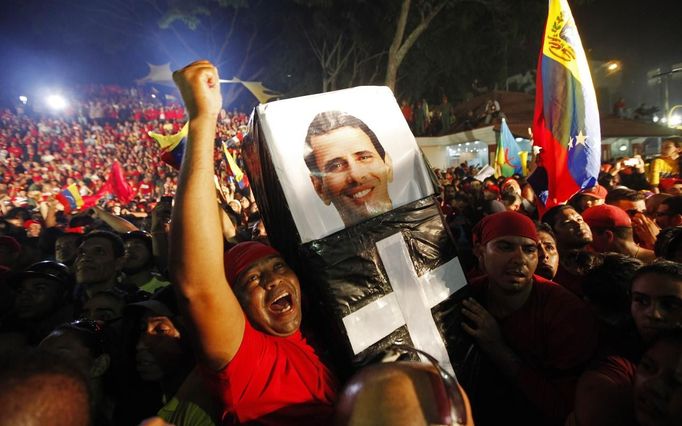 Supporters of Venezuelan President Hugo Chavez hold a mock coffin with a portrait of opposition candidate Henrique Capriles, as they cheer for Chavez outside Miraflores Palace in Caracas October 7, 2012. Venezuela's socialist President Chavez won re-election in Sunday's vote with 54 percent of the ballot to beat opposition challenger Henrique Capriles. REUTERS/Tomas Bravo (VENEZUELA - Tags: POLITICS ELECTIONS) Published: Říj. 8, 2012, 5:51 dop.