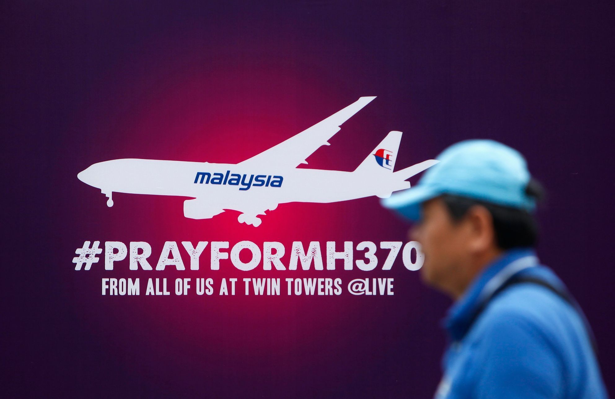 A tourist walks past a signboard saying &quot;Pray for MH370&quot; in front of the Kuala Lumpur City Center