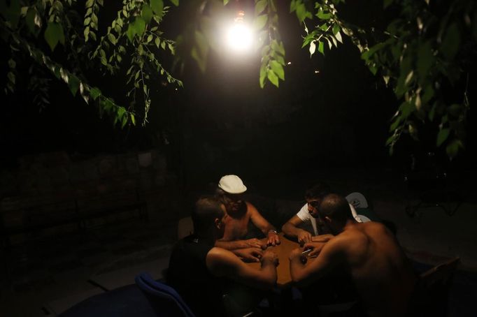 Relatives of Antonio Gabarri play domino by the light of a bulb hanging from a tree next to the remains of what used to be Gabarri's home at the Spanish gypsy settlement of Puerta de Hierro outside Madrid July 18, 2012. Fifty-four families have been living in Puerta de Hierro, on the banks of the Manzanares river for over 50 years. Since the summer of 2010, the community has been subject to evictions on the grounds that the dwellings are illegal. Families whose houses have been demolished, move in with relatives whose houses still remain while the debris keeps piling up around them as more demolitions take place. Picture taken July 18, 2012. REUTERS/Susana Vera (SPAIN - Tags: SOCIETY) ATTENTION EDITORS - PICTURE 26 OF 31 FOR PACKAGE 'GYPSY SITE DEMOLISHED' SEARCH 'GYPSY SITE' FOR ALL IMAGES Published: Lis. 5, 2012, 4:12 odp.